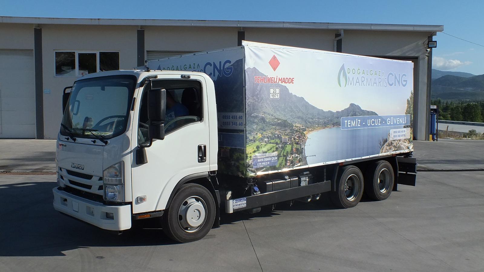 Isuzu truck with MARMARİS CNG scenic lake graphics parked at CNG facility with storage tanks