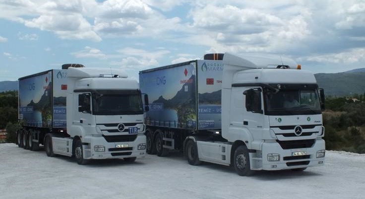 Two white Mercedes trucks with matching blue CNG trailers featuring mountain lake graphics