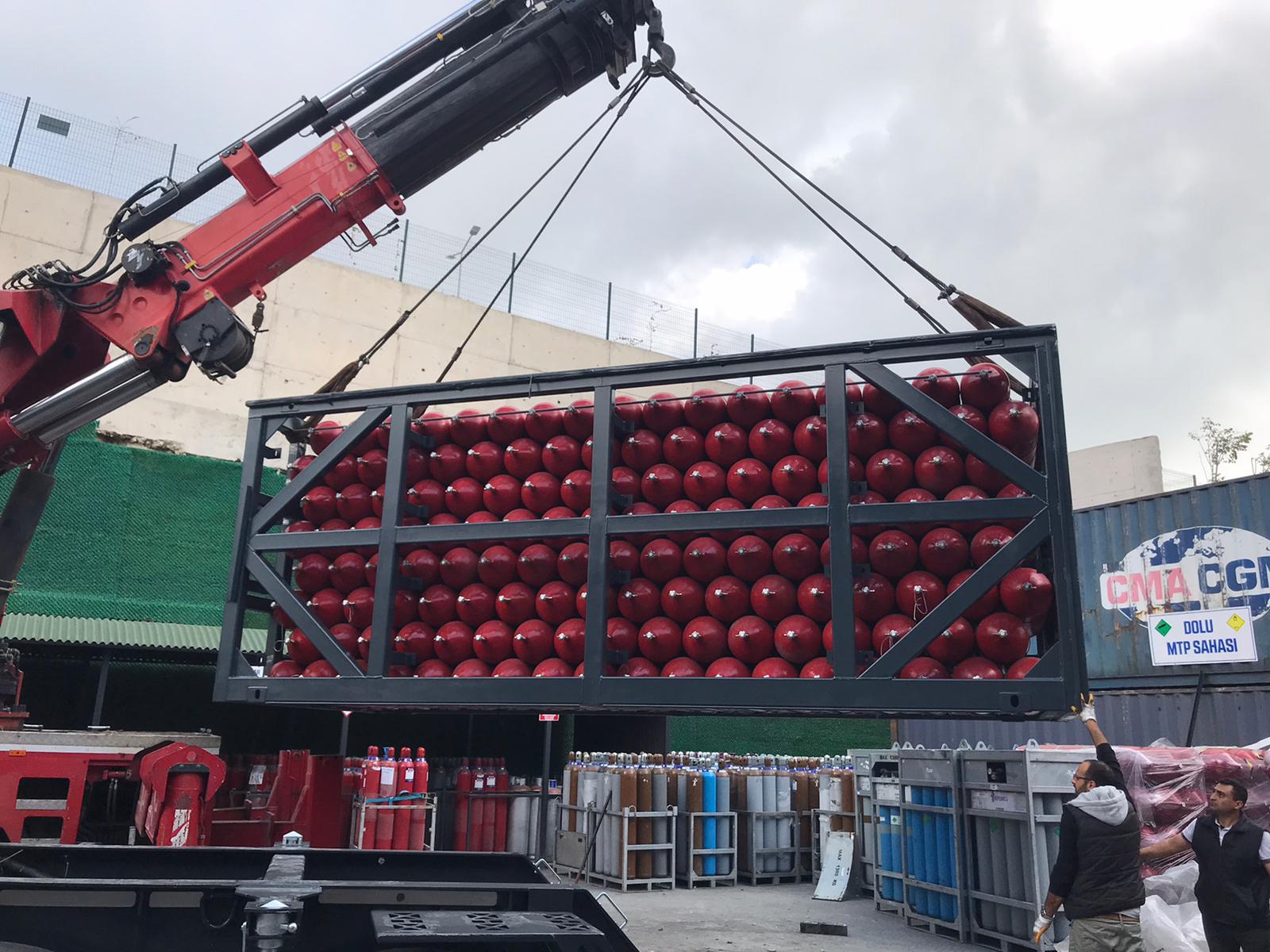 Crane lifting black MEGC frame filled with red CNG cylinders at manufacturing facility